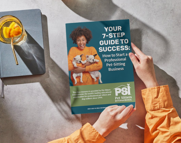 Hands of person holding a book with the title Your 7-Step Guide to Success, How to Start a Professional Pet-Sitting Business