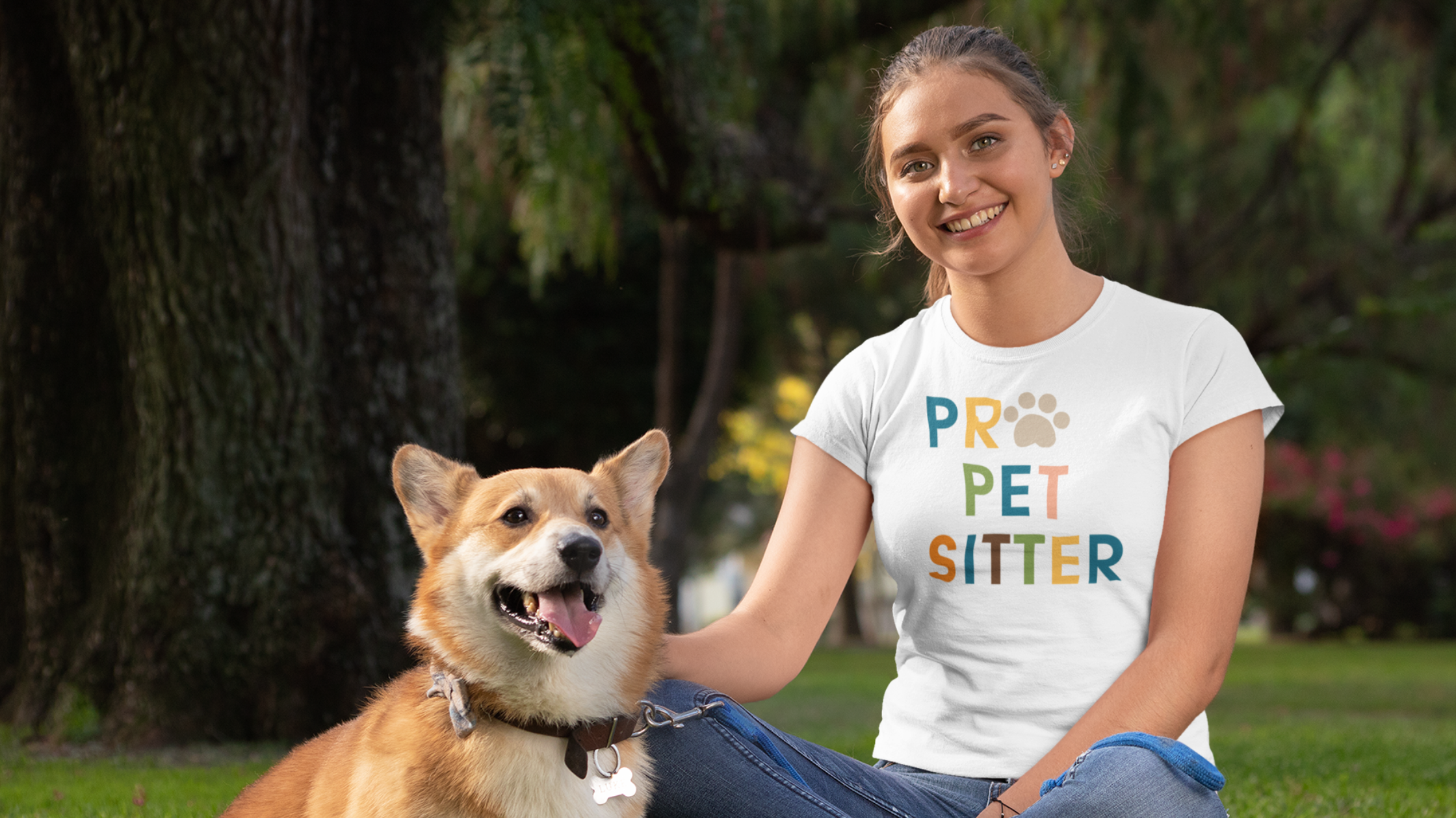 Starting a pet sitting business 2025 Young adult woman wearing denim jeans and a white t-shirt that says PRO PET SITTER sitting in the grass with a Corgi dog with brown and white fur